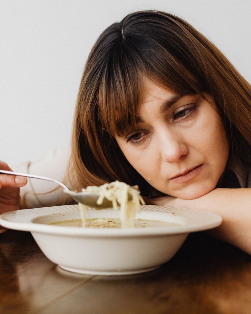 Mulher olhando um prato de sopa tristemente.