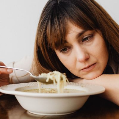 Mulher olhando um prato de sopa tristemente.